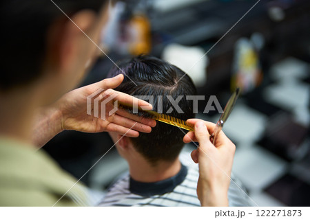 Barber skillfully cuts hair with precision in modern barbershop setting 122271873
