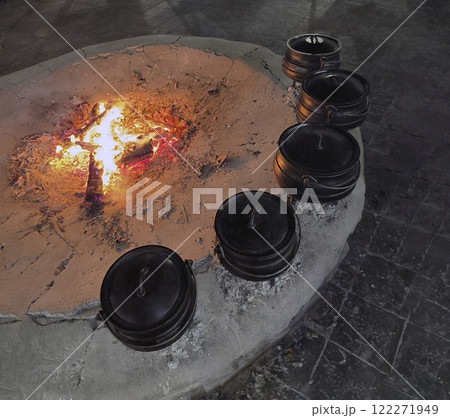Five cast iron pots with lids sit over an open fire and coals. 122271949