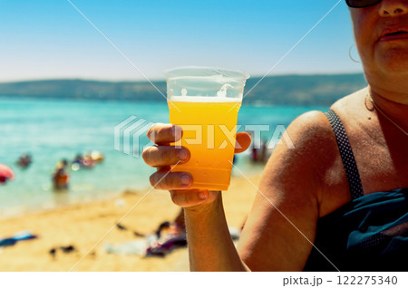 A woman is holding a plastic cup of beer on a beach. A woman is holding a plastic cup of beer on a beach. 122275340