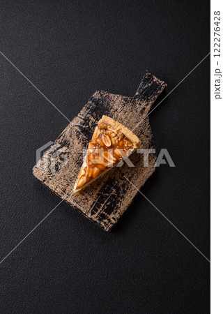 Delicious fresh cheesecake caramel peanut cake with cream and nuts on a ceramic plate on a dark concrete background 122276428