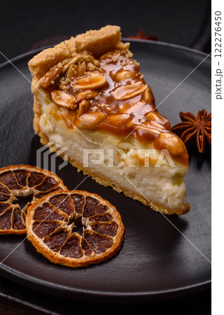 Delicious fresh cheesecake caramel peanut cake with cream and nuts on a ceramic plate on a dark concrete background 122276450