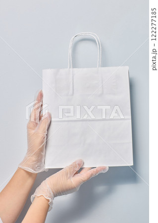 Hands Gently Holding a Clean and Pristine White Shopping Bag while Wearing Protective Gloves 122277185