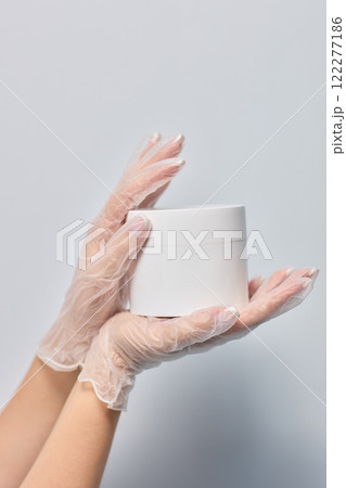 Hands in Gloves Holding a White Container for Safety and Cleanliness in a Professional Setting Hands in Gloves Holding a White Container for Safety and Cleanliness in a Professional Setting 122277186