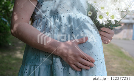 A pregnant woman is holding a bouquet of white flowers while wearing a blue dress A pregnant woman is holding a bouquet of white flowers while wearing a blue dress 122277252
