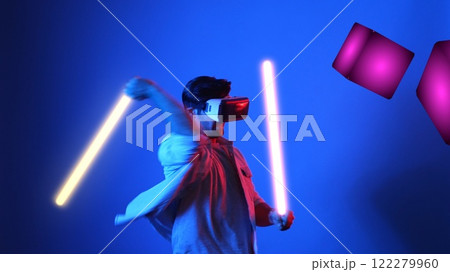 Gamer playing game while holding neon sword and wearing VR glasses. Apparatus. 122279960