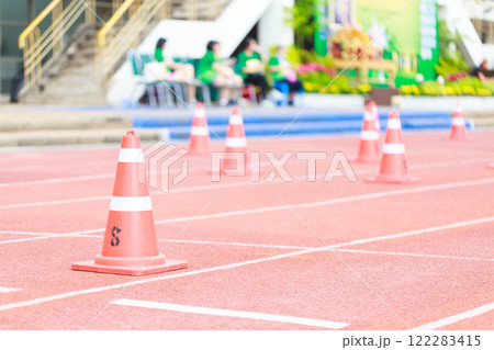 Orange traffic cones on red running track, marking lanes for sports event. vibrant colors create lively atmosphere, perfect for competitions and athletic activities Orange traffic cones on red running track, marking lanes for sports event. vibrant colors create lively atmosphere, perfect for competitions and athletic activities 122283415