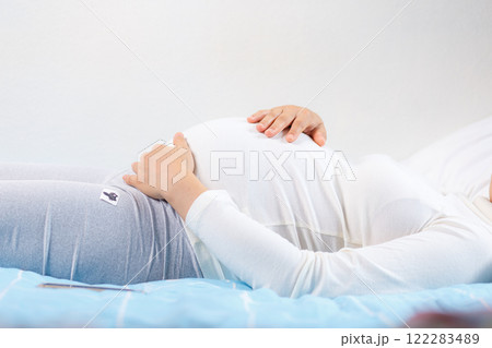 pregnant woman gently cradles her belly while lying on bed, showcasing beauty of motherhood and anticipation pregnant woman gently cradles her belly while lying on bed, showcasing beauty of motherhood and anticipation 122283489