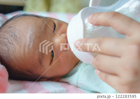 newborn baby lying on soft blanket is being fed milk from bottle by caregiver hand, showcasing tender care and nurturing 122283595