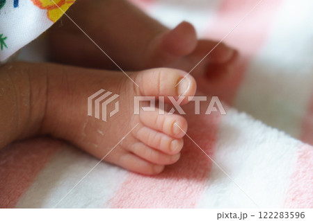 Close up of newborn baby feet resting on soft pink and white striped blanket, showcasing delicate skin and tiny toes in peaceful and tender moment 122283596