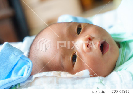 close up of newborn baby lying on soft surface, wearing light green outfit with blue blanket nearby, expressing curiosity and innocence 122283597
