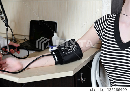 Medical professional checks blood pressure of a young woman in a clinic while wearing masks for safety during a health appointment 122286499