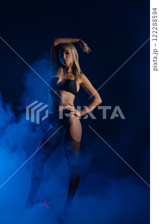 Stylish model posing confidently in low light with blue smoke background Stylish model posing confidently in low light with blue smoke background 122288594