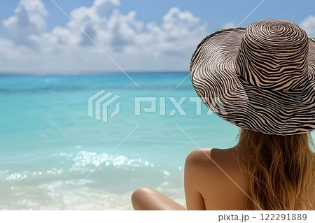 A serene view from behind of a woman sitting on a pristine white sandy beach, gazing at the turquoise ocean on a sunny day in the Maldives.  122291889