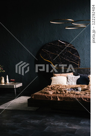 Modern bedroom with a black wall. Bed is covered with a brown comforter and pillows. Vase with flowers is on a table Modern bedroom with a black wall. Bed is covered with a brown comforter and pillows. Vase with flowers is on a table 122292484