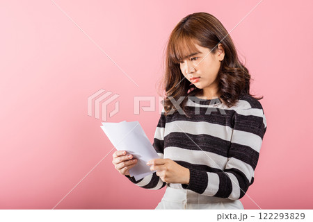 Portrait of beautiful Asian young woman sad tired strain holding paper calculating bills on hand, female person problem she hold worried over bill, studio shot isolated on pink background 122293829