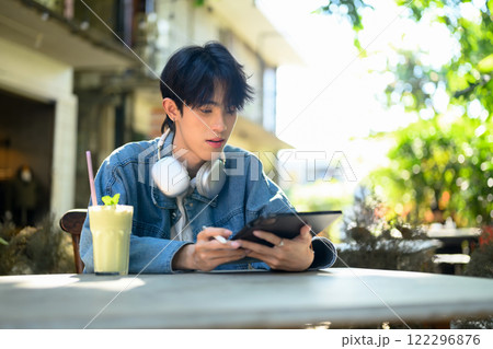 Young stylish man sitting at cafe table with a refreshing beverage and using digital tablet 122296876