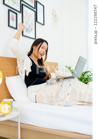 Vertical image of beautiful young Asian woman lean on bed with stretch lazily and relax in bedroom. 122298547