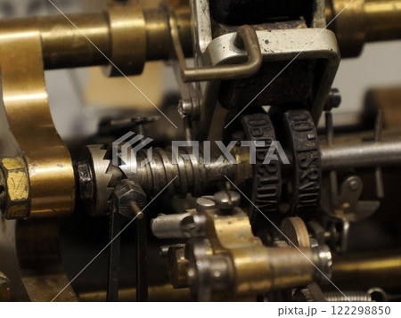 A detailed close-up shot reveals the intricate, brass and steel mechanisms of an antique printing press, emphasizing the texture and worn quality of the machine's components. A detailed close-up shot reveals the intricate, brass and steel mechanisms of an antique printing press, emphasizing the texture and worn quality of the machine's components. 122298850