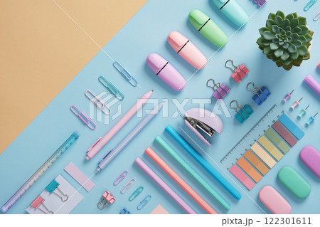 Stationery with markers, felt-tip pens, paper clips, erasers, stapler, pastel-colored stickers neatly arranged on a light blue and beige background. Space for text. 122301611