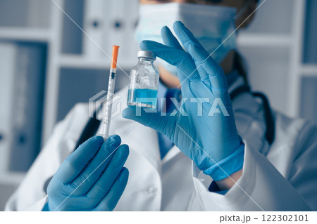 A medical professional in gloves holds a vaccine vial and syringe, preparing for immunization to ensure patient safety and health in a sterile environment with essential clinical equipment 122302101