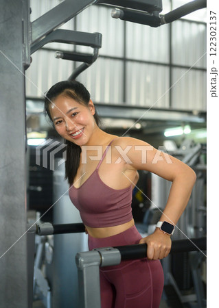 Smiling female athlete doing push ups on parallel bars in the gym 122302137