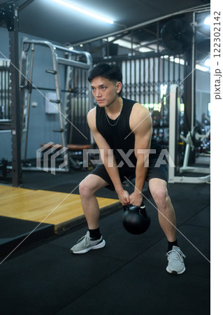 Handsome sportsman exercising with kettle bell at gym. Fit, sports and healthy lifestyle concept Handsome sportsman exercising with kettle bell at gym. Fit, sports and healthy lifestyle concept 122302142