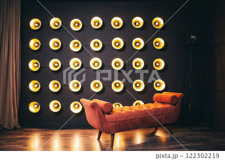 orange sofa against a wall incandescent lamps. photo zone with floor lamps the wall and a soft chair orange sofa against a wall incandescent lamps. photo zone with floor lamps the wall and a soft chair 122302219