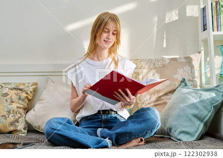Portrait of female student sitting on couch with notebook, studying at home 122302938