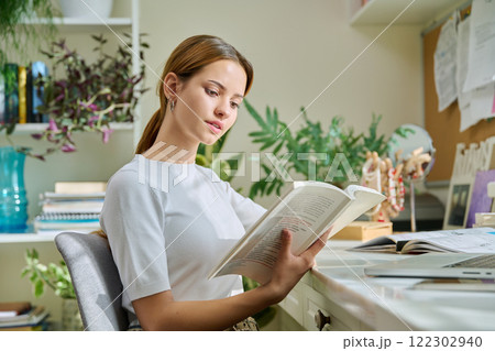 Young teenage female reading book, novel, fiction educational literature at home 122302940