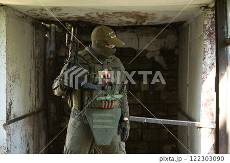 A tactical operator dressed in military gear and a cap stands inside an abandoned building, holding a rifle. A tactical operator dressed in military gear and a cap stands inside an abandoned building, holding a rifle. 122303090