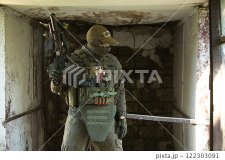 A tactical operator dressed in military gear and a cap stands inside an abandoned building, holding a rifle. A tactical operator dressed in military gear and a cap stands inside an abandoned building, holding a rifle. 122303091
