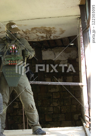 A tactical operator dressed in military gear and a cap stands inside an abandoned building, holding a rifle. A tactical operator dressed in military gear and a cap stands inside an abandoned building, holding a rifle. 122303095