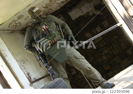 A tactical operator dressed in military gear and a cap stands inside an abandoned building, holding a rifle. 122303096