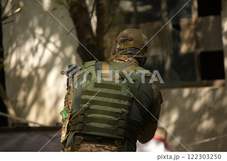 Tactical soldier with a scoped rifle preparing to enter an abandoned building, showcasing precision and focus during an outdoor operation.  122303250