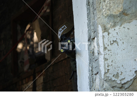 A tactical operator in military gear takes cover behind a moss-covered stone wall while aiming through the scope of a rifle. A tactical operator in military gear takes cover behind a moss-covered stone wall while aiming through the scope of a rifle. 122303280