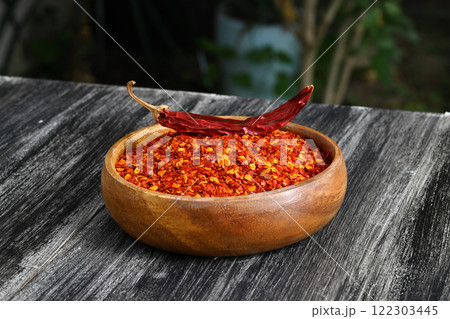 Wooden bowl with crushed chili pepper and fresh red chili pepper on old table. Selective focus. 122303445