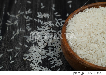 Raw white rice on wooden background. Long uncooked rice in wooden plate. Natural organic food. Traditional Asian cereal culture. 122303448