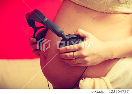 Woman with headphones on pregnant belly Woman with headphones on pregnant belly 122304727