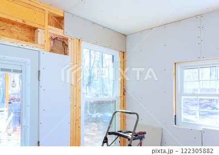 Installing gypsum drywall in space for improved energy efficiency through large windows. 122305882