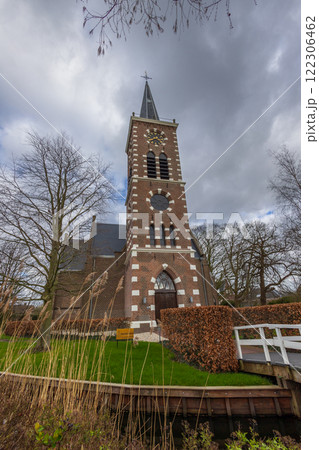 A picturesque brick church with a tall spire, surrounded by bare trees, viewed from a wooden footbridge. A picturesque brick church with a tall spire, surrounded by bare trees, viewed from a wooden footbridge. 122306462