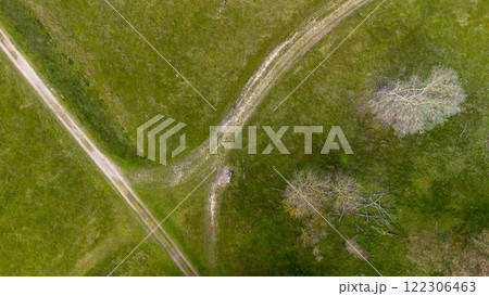 Aerial view of a grassy landscape with intersecting dirt paths, surrounded by scattered trees and open green fields, capturing a tranquil and natural outdoor scene. Aerial view of a grassy landscape with intersecting dirt paths, surrounded by scattered trees and open green fields, capturing a tranquil and natural outdoor scene. 122306463