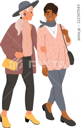 Two fashionable women, one older with gray hair and a hat, and one younger with darker skin, are walking together arm in arm, enjoying a conversation and showcasing their individual styles 122307043