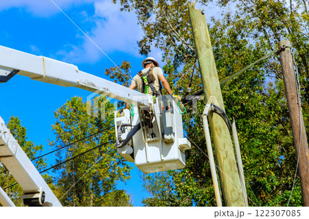 Technician handles wiring on power pole using lift, set against home 122307085
