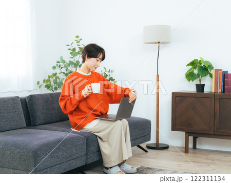 リビングルームでノートパソコンを見ながらくつろぐミドル女性 122311134