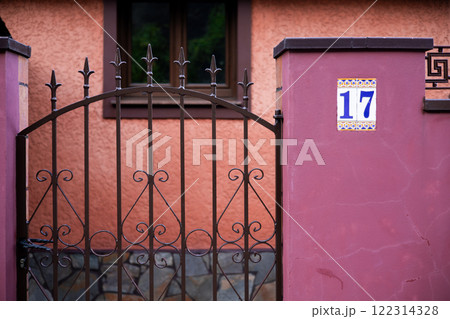 Ornate iron gate and pink wall with number 17 in spanish style architecture Ornate iron gate and pink wall with number 17 in spanish style architecture 122314328