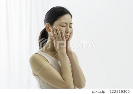 両頬を抑える白背景の困った顔の若い女性　肌荒れ 122316300