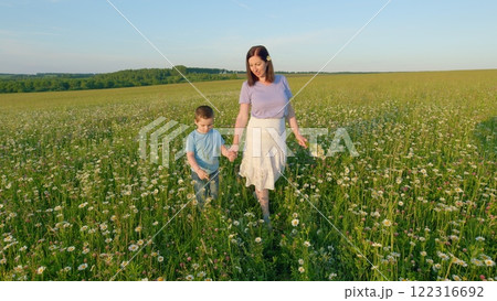 Happy Family With Child Going Among Meadow. Family Outdoors Walking On Wild Flower Field With Little Boy. Mother And Son Are Walking Through Meadow. Gimbal shot. Happy Family With Child Going Among Meadow. Family Outdoors Walking On Wild Flower Field With Little Boy. Mother And Son Are Walking Through Meadow. Gimbal shot. 122316692