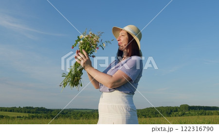 Portrait Of Young Woman With Bouquet Smelling Wild Flowers On Summer Field And Smiling. Leisure Activity On Outdoor Nature. Enjoying A Nature. Moves slowly. Portrait Of Young Woman With Bouquet Smelling Wild Flowers On Summer Field And Smiling. Leisure Activity On Outdoor Nature. Enjoying A Nature. Moves slowly. 122316790
