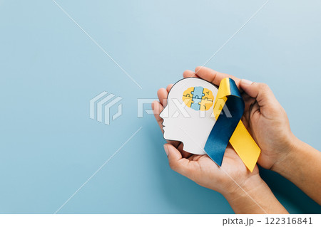 Hands holding a head with puzzle pieces and a ribbon. Celebrating Down Syndrome Day 122316841