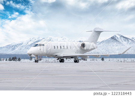 White luxury executive airplane taxiing on airport taxiway in winter on the background of high picturesque snow capped mountains White luxury executive airplane taxiing on airport taxiway in winter on the background of high picturesque snow capped mountains 122318443